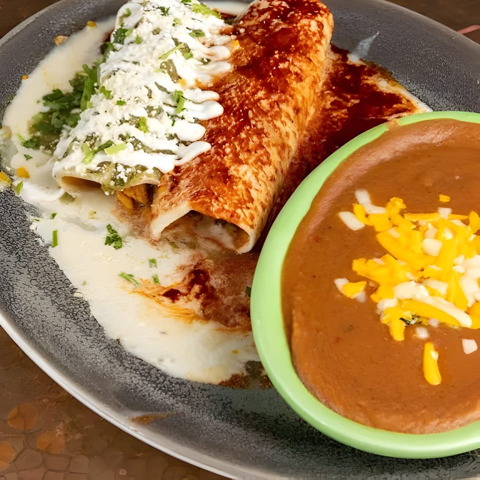 Two enchiladas, one green and one red, with a side of refried beans topped with cheese.