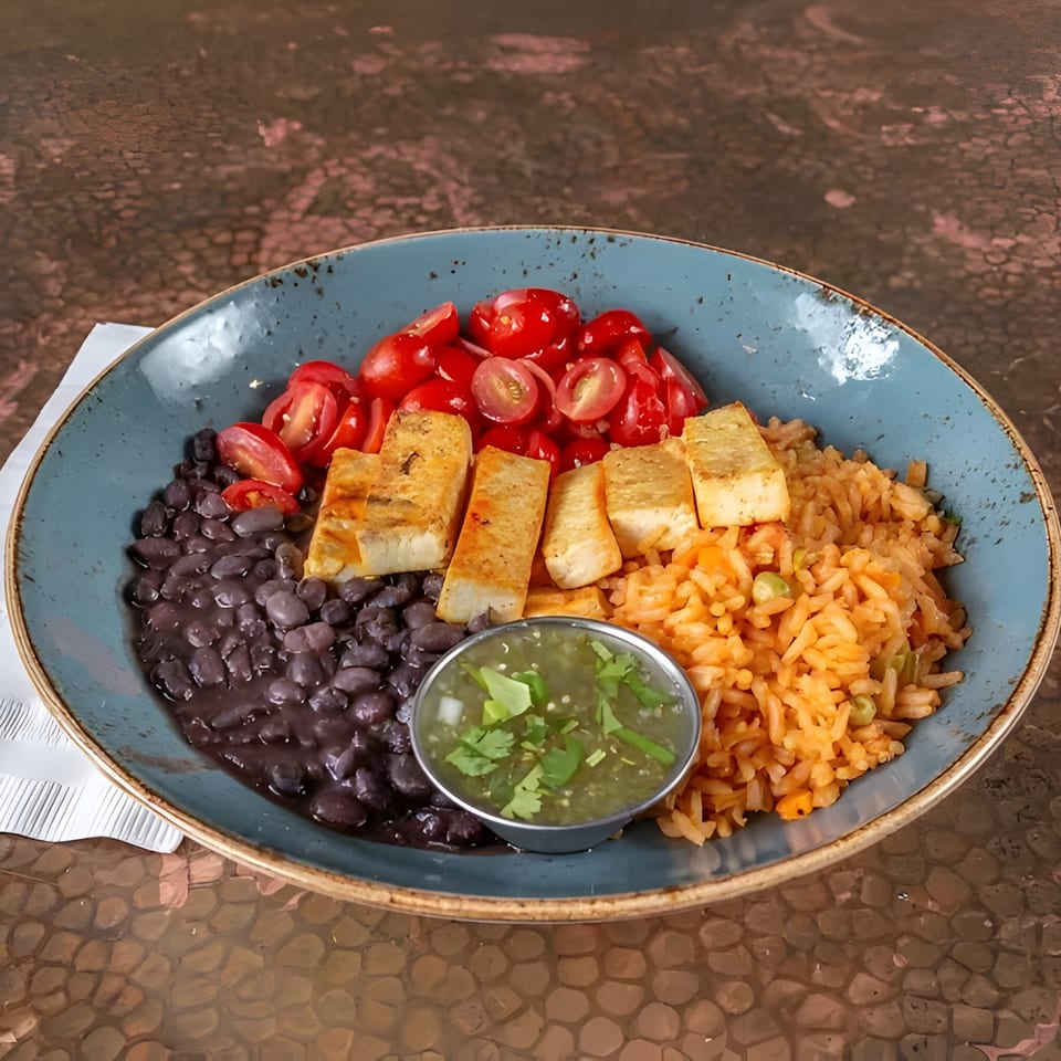 A Mexican dish with black beans, rice, grilled tofu, cherry tomatoes, and green salsa.