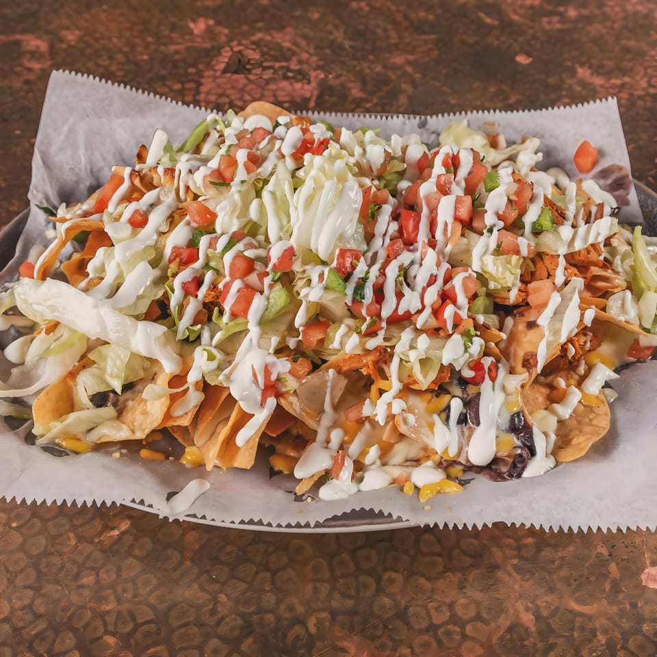 A large plate of Buenatarde Tequila y Mezcal's Mexican nachos, topped with cheese, meat, and vegetables.