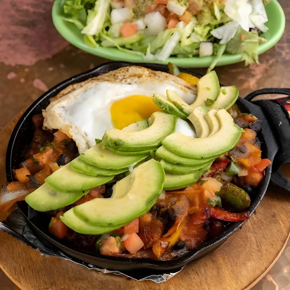 Sizzling Mexican fajitas with a fried egg and avocado slices, served with a side salad.