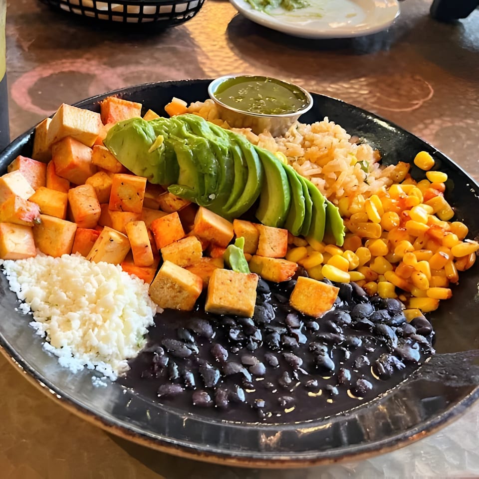 A colorful Mexican bowl with avocado, rice, corn, black beans, cotija cheese, and tofu.
