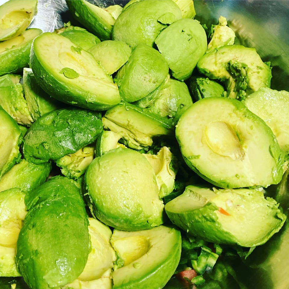 Close-up of many fresh, ripe avocado halves and chunks in a metal bowl, ready for guacamole.
